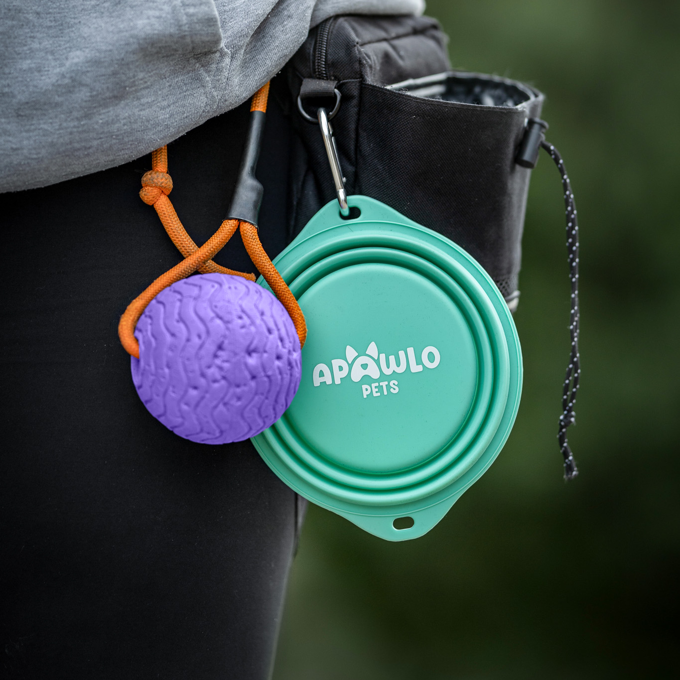 Purple ball and teal container attached to a person's pocket with a blurred green background
